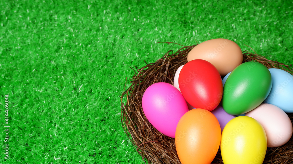 Multi colored easter eggs in birds nest on green grass lawn background closeup view selective focus with copy space. Easter holiday banner, card, poster, header, voucher, invitation template