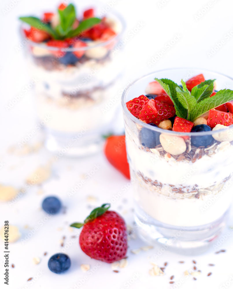 Healthy breakfast of strawberry parfait made with fresh fruit, yogurt, blueberries, flax seeds and muesli, white background. Small depth of field with selective focus on the glass jar in front. Healthy breakfast of strawberry parfait made with fresh fruit, yogurt, blueberries, flax seeds and muesli, white background. Small depth of field with selective focus on the glass jar in front.