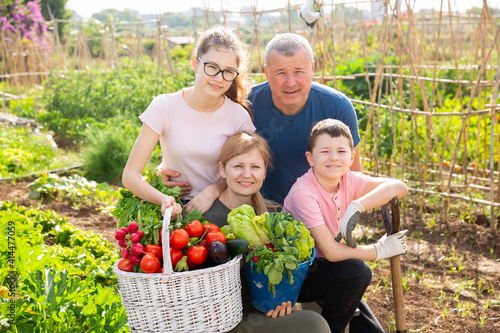 Portrait of couple with boy and teen girl posing with fresh harvest on small agricultural family farm