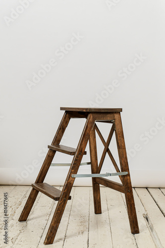 High wooden stepladder chair on white photographic background on white wooden floor. Space for text on top.