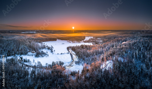 Warm sunrise over snowy countryside landscape. Pine forest covered in fog waves. Drone aerial view. © Viesturs