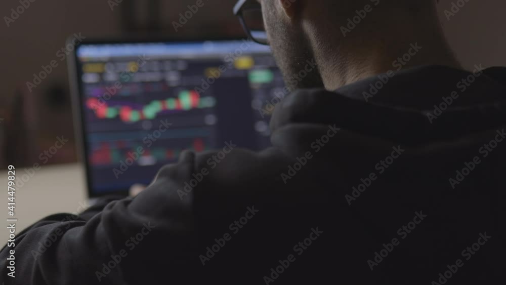 Caucasian man works on his investment. Investor, financial concept. Stock chart. Attractive man invests on stock market from his workplace or office. View from behind. Laptop screen. Cinematic shot Caucasian man works on his investment. Investor, financial concept. Stock chart. Attractive man invests on stock market from his workplace or office. View from behind. Laptop screen. Cinematic shot
