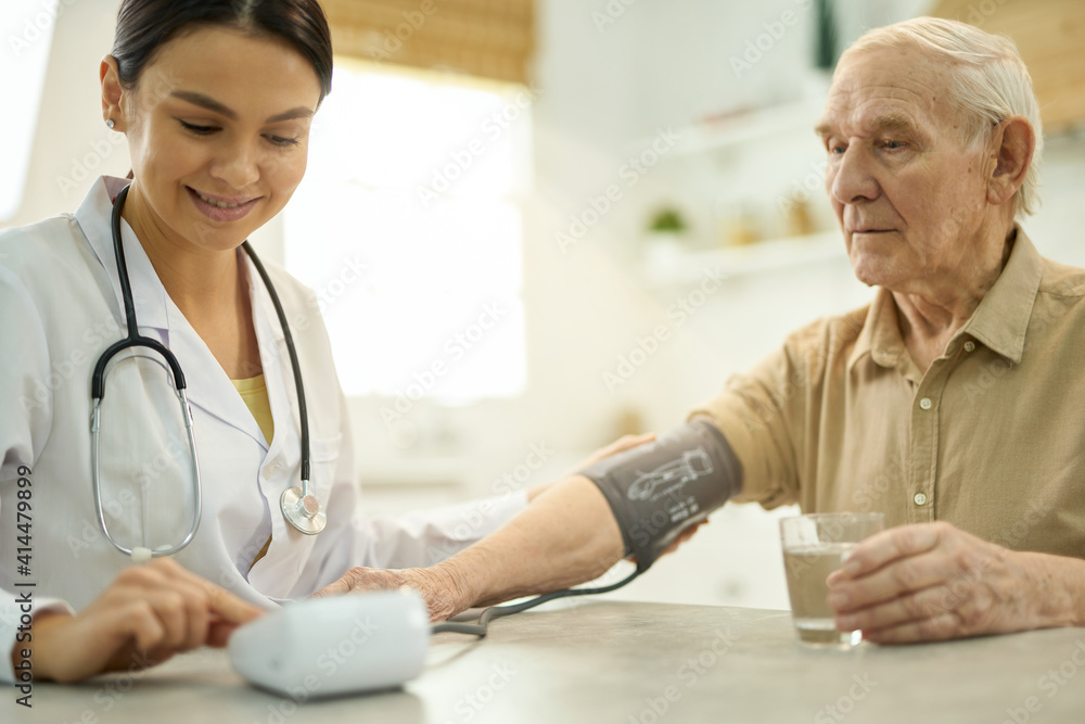 Obraz premium Easy-going doctor using a manometer while examining her aged patient