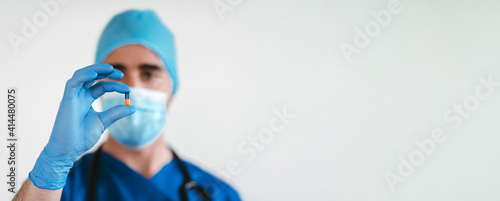 Selective focus on a pill in the hands of a doctor wearing a mask and a uniform © Iker