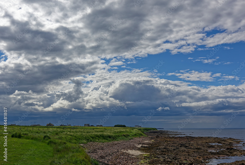 Fields running down to the shingle and rocky beach at John O'Groats with scattered houses and farm Buildings seen in the distance under a heavy sky. Fields running down to the shingle and rocky beach at John O'Groats with scattered houses and farm Buildings seen in the distance under a heavy sky.