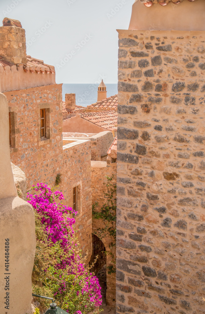 Φωτογραφία narrow alley with purple bougainvillea hanging between the plastered houses with