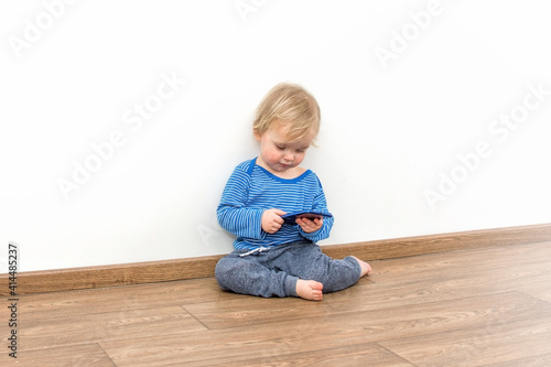 Little baby boy sitting on the floor at home and playing with smartphone.
