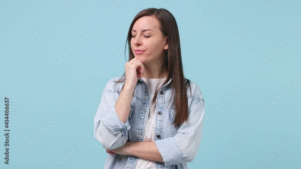 Puzzled pensive long hair brunette young woman 30s years old in denim jacket white t-shirt looking aside up put hand prop up on chin isolated on pastel blue background studio. People lifestyle concept Puzzled pensive long hair brunette young woman 30s years old in denim jacket white t-shirt looking aside up put hand prop up on chin isolated on pastel blue background studio. People lifestyle concept