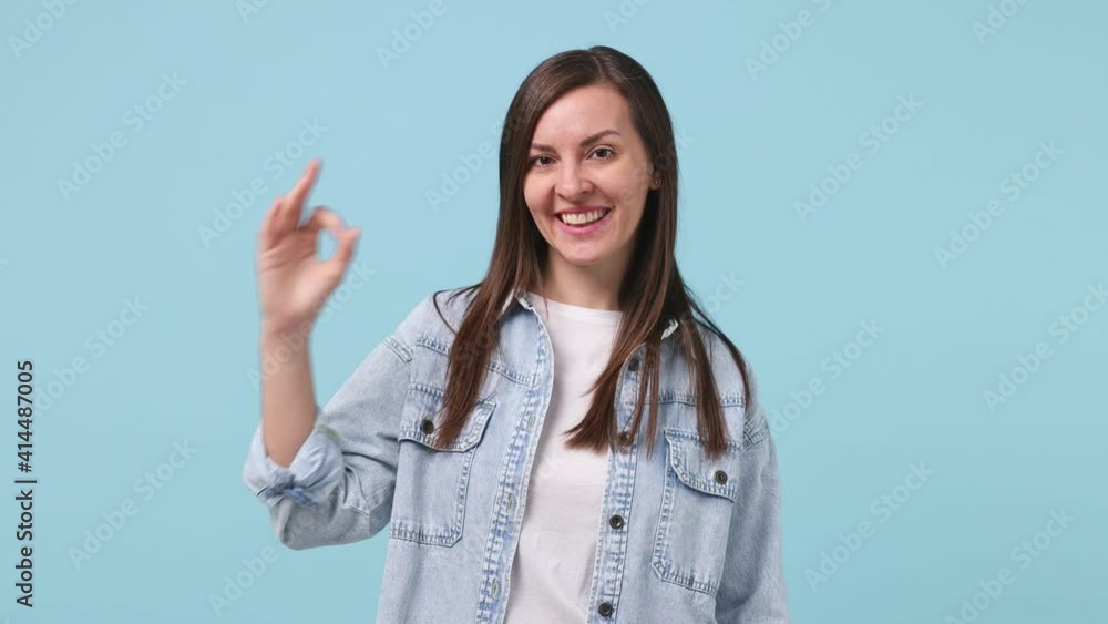 Smiling cheerful cute young woman 30s years old in denim jacket white t-shirt posing isolated on pastel blue background studio. People lifestyle concept. Looking camera showing okay ok fingers gesture Smiling cheerful cute young woman 30s years old in denim jacket white t-shirt posing isolated on pastel blue background studio. People lifestyle concept. Looking camera showing okay ok fingers gesture