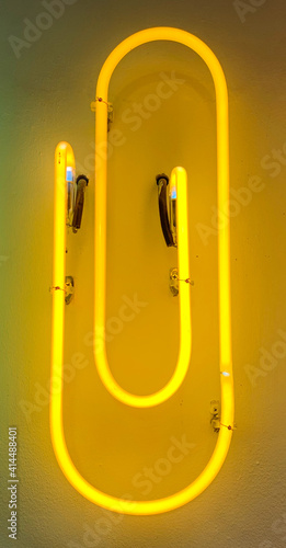 Yellow office clip shape neon light installed on white wall