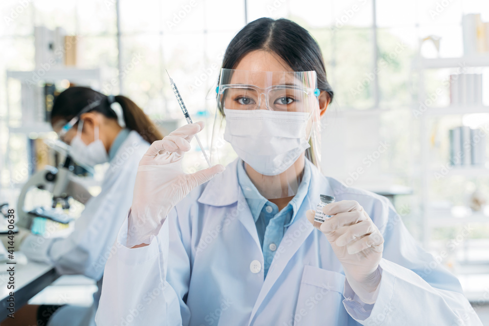 Successful young female medical researcher and scientist wearing labcoat standing in laboratory while working on developing covid-19 vaccine holding injection and bottle Successful young female medical researcher and scientist wearing labcoat standing in laboratory while working on developing covid-19 vaccine holding injection and bottle