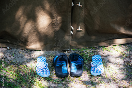 Two pairs of women's and men's flip flops near tourist tent in the forest. Family trip, romance concept. Selective focus.