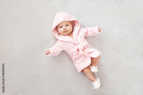 Baby girl in a Terry robe and diaper after bathing. Kid in a hood. Cute happy laughing baby girl in pink soft robe after bath. Baby in a clean and dry towel.