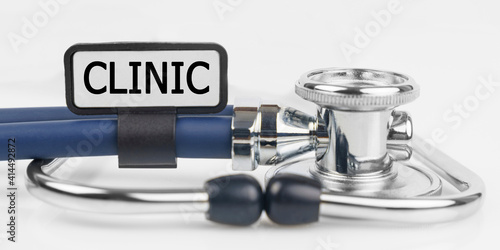 On the white surface lies a stethoscope with a plate with the inscription - CLINIC
