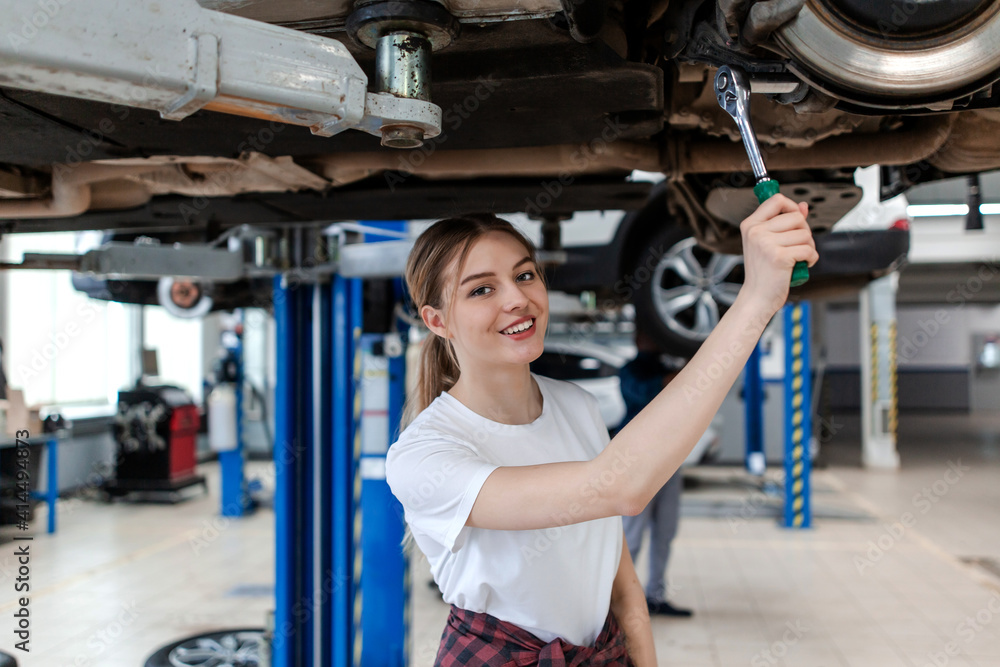 Fototapeta premium Car mechanic girl making car repairs on a lift in a car service station