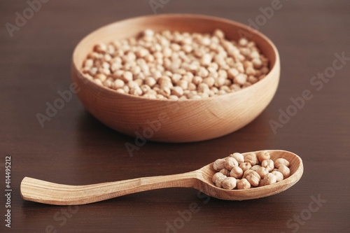 Dry chickpeas in a wooden plate and spoon on a brown wooden background. Copy, empty space for text