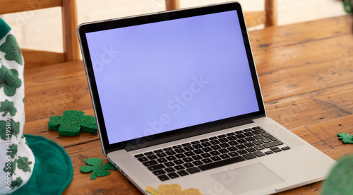 Laptop computer on a wooden dining table with shamrock decorations for st patrick's day