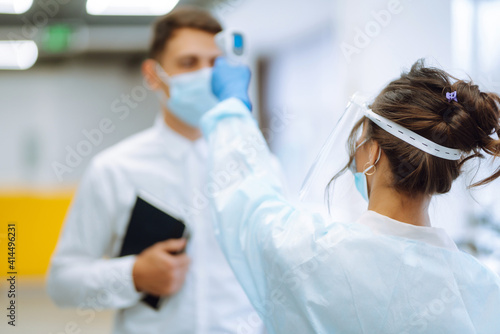 Temperature screening office workers. Disease control expert in visor and protective gloves  with an Infrared thermometer equipment to check the temperature at office during pandemic in quarantine. 