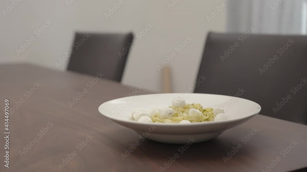 Slow motion man add spices to pesto fettuccine in white pasta plate on walnut table Slow motion man add spices to pesto fettuccine in white pasta plate on walnut table