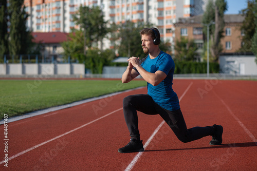 Muscular guy with earphones doing lunges