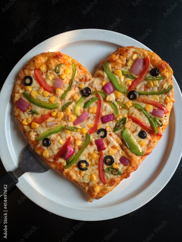 A delicious looking heart shaped vegetable cheese pizza served on a white round plate over a black surface table at a southeast Asian restaurant