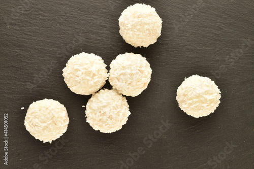 Several round white candies with coconut flakes on a slate board, close-up, top view.