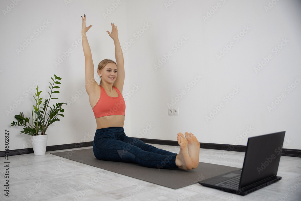 Happy smiling young female in sportswear watching aerobics online videos on laptop exercising, enjoying fitness at home