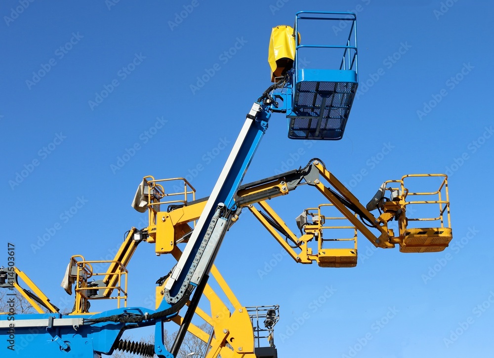 Blue and yellow aerial work platform against clear blue sky Blue and yellow aerial work platform against clear blue sky