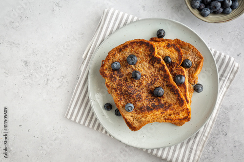Flat lay of three slices of french toast with blueberries on a plate on grey background, copy space on the left