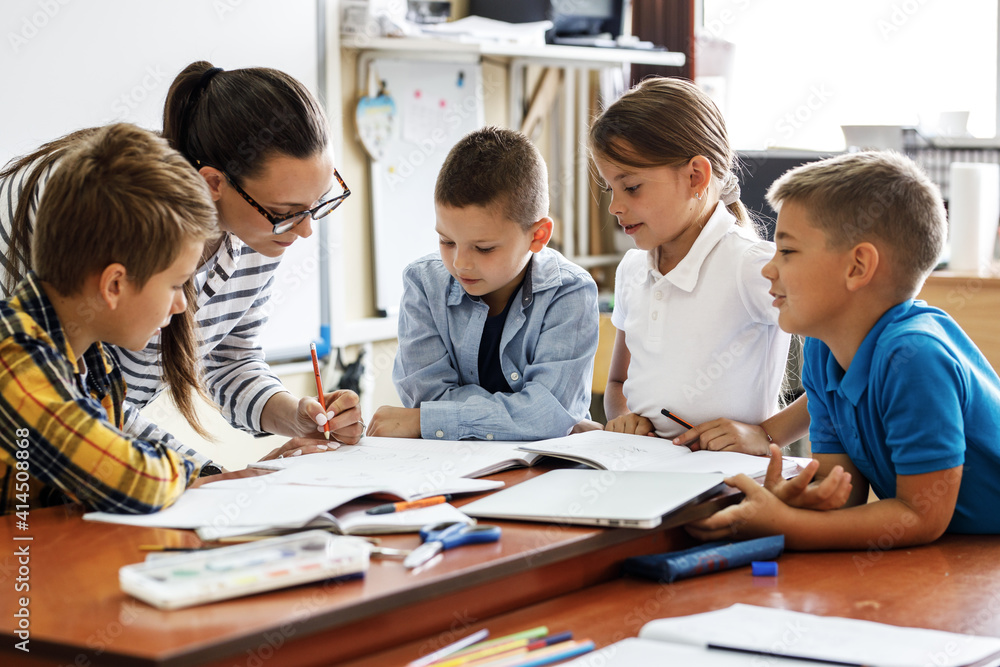 Female teacher helps school kids to finish they lesson.They sitting all together at one desk.
Female teacher helps school kids to finish they lesson.They sitting all together at one desk.