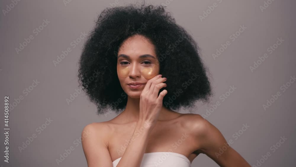 african american woman applying golden eye patches isolated on grey african american woman applying golden eye patches isolated on grey