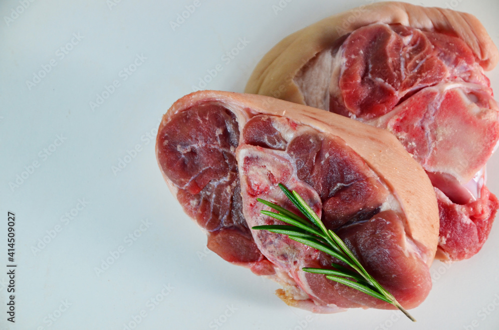 pieces of raw pork steaks, with ingredients for cooking, served on woodenboard. with rosemary, cherry tomatoes, black pepper and olive oil on the table Concept of food preparation on white background