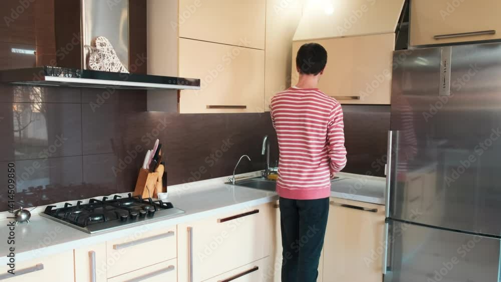 A man taking a cup, filling it with water and drinking it on the modern kitchen A man taking a cup, filling it with water and drinking it on the modern kitchen