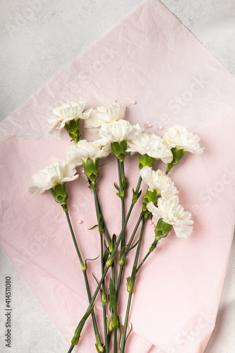 Bouquet of white carnations on pink paper