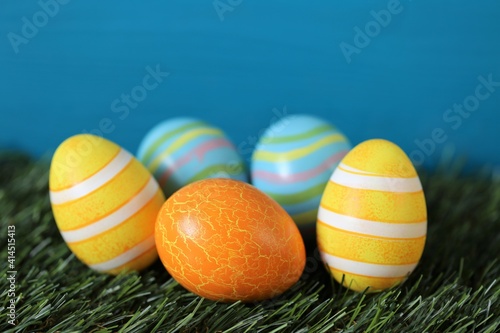 Easter holiday.Multicolored striped easter eggs set on green grass on bright turquoise background..Spring festive easter background. copy space. Easter egg hunt