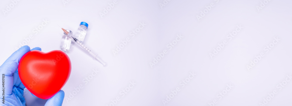a hand in a medical glove holds an ampoule containing the covid-19 vaccine, invented to prevent the spread of the virus around the world. mask with a red heart on a white background Copy Space a hand in a medical glove holds an ampoule containing the covid-19 vaccine, invented to prevent the spread of the virus around the world. mask with a red heart on a white background Copy Space