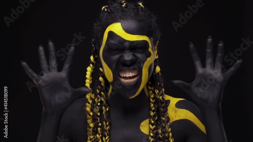 Face art. Screaming snarling wild woman with black and yellow body paint. Young african girl with colorful bodypaint. An amazing afro american model with yellow makeup. photo