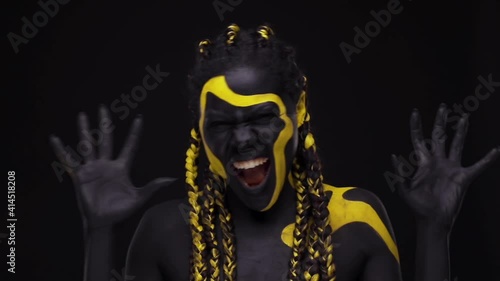 Face art. Screaming snarling wild woman with black and yellow body paint. Young african girl with colorful bodypaint. An amazing afro american model with yellow makeup. photo