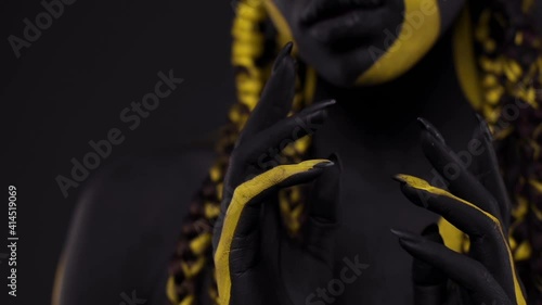 Face art. Woman with black and yellow body paint. Young african girl with colorful bodypaint. An amazing afro american model with yellow makeup. photo