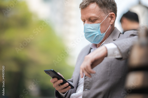 professional adult businessman wearing surgical face mask to protect of coronavirus covid-19, business worker new normal lifestyle on the background of urban city skyscraper, person in business suit