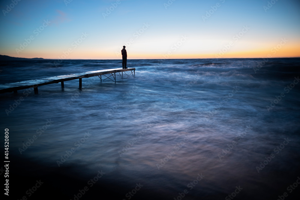 Fototapeta premium person walking on the pier at sunset