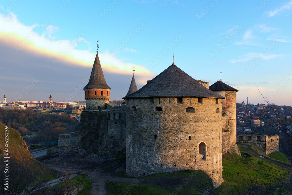 Scenic landscape photo of ancient stone fortress in the city of Kamianets-Podilskyi during winter sunset. Panoramic dramatic sunset sky. Famous touristic place and romantic travel destination. Ukraine