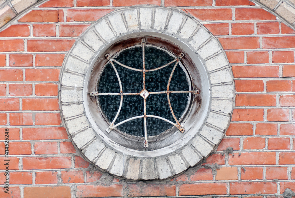 round window with grille on the brick wall closeup