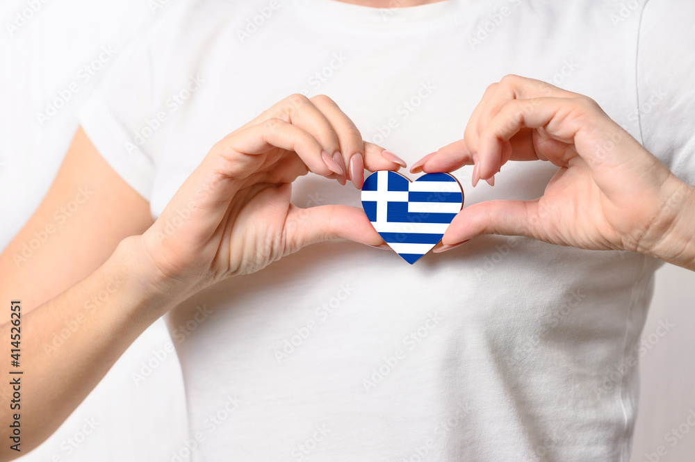 Love Greece. The girl holds a heart in the form of the flag of Greece on her chest. Greek patriotism concept