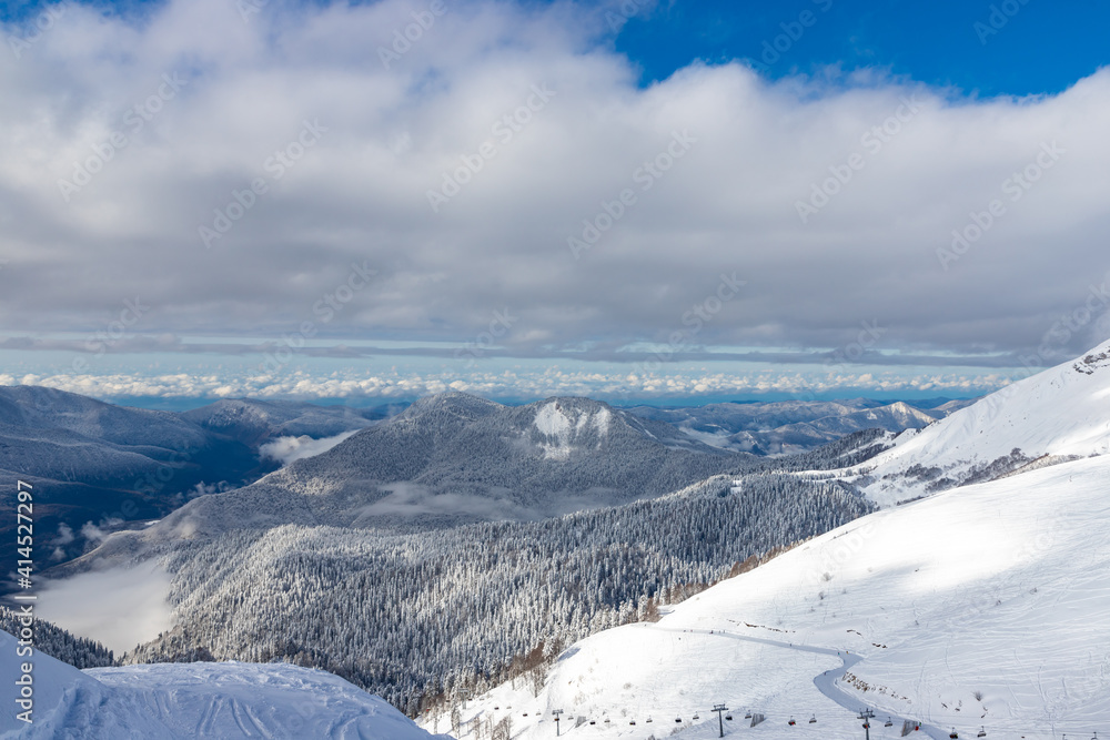 Obraz premium Snow-covered mountains and ski slopes with clouds on background. Ski resort Roza Khutor. Sochi. Russia.