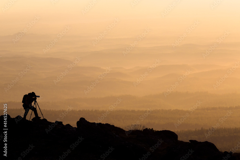 silhouette of landscape photographer who shoots in mountains during sunset with mirror camera and tripod