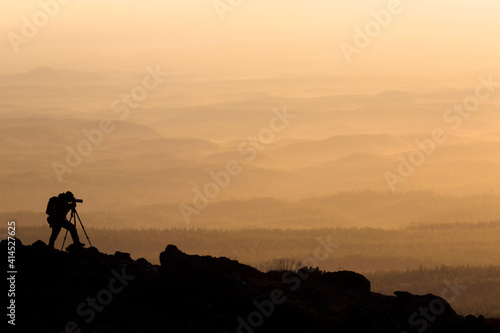 silhouette of landscape photographer who shoots in mountains during sunset with mirror camera and tripod