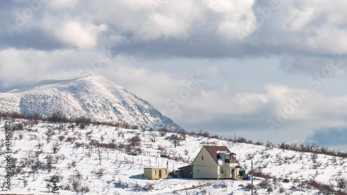 Gray clouds over small house in snowy mountains in cold winter, time lapse