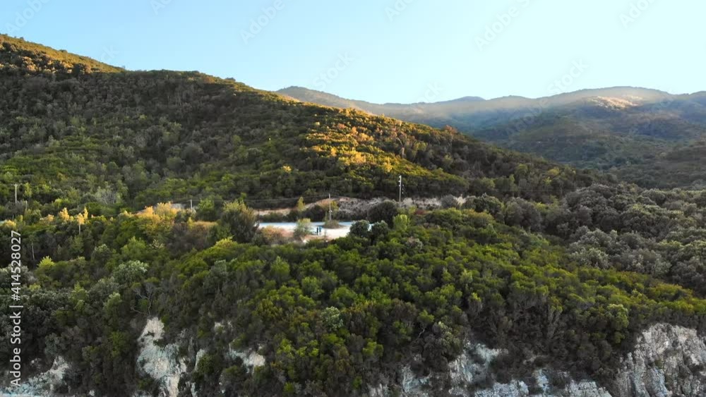 Aerial drone view of the Aegean sea rocky coast with green hills neat the shore, observation point with a couple on the side of a road in Greece Aerial drone view of the Aegean sea rocky coast with green hills neat the shore, observation point with a couple on the side of a road in Greece