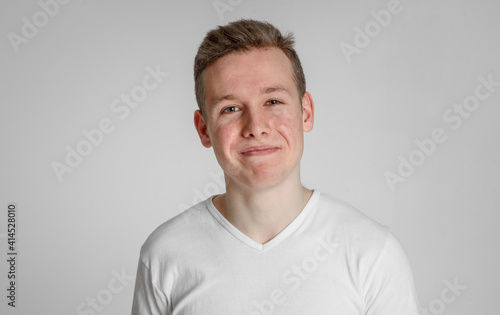 
teen guy looking into the frame surprised can't believe raised eyebrows
 and sincerely smiling with teeth on a white background in a white T-shirt